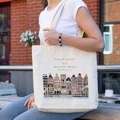 a woman is sitting on a bench holding a tote bag that has an image of buildings