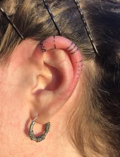 a woman with some piercings on her ear and behind her ear is a pair of scissors