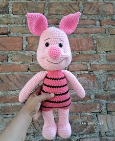 a crocheted pig stuffed animal in pink and black striped shirt sitting next to a brick wall