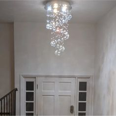 an empty hallway with a chandelier hanging from the ceiling and two doors leading to another room