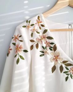 a white dress with pink flowers on it hanging from a wooden hanger next to a wall