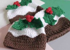 two crocheted hats with holly leaves on them, one is brown and the other is white