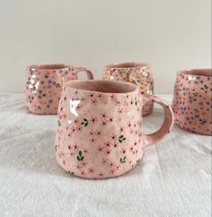 four pink coffee mugs sitting on top of a white table covered in confetti