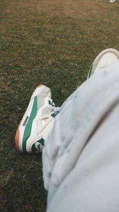 a person's feet with green and white tennis shoes on the grass in front of a soccer field