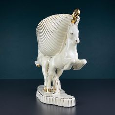 a white and gold horse figurine sitting on top of a black table next to a blue wall