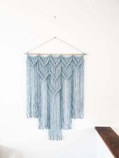 a blue wall hanging with fringes and beads on a wooden shelf next to a white wall