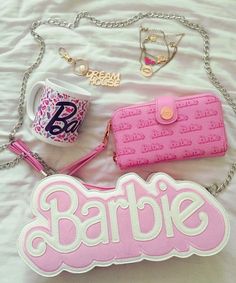 a pink purse and some other items are laying on a white sheet with the word barbie written across it