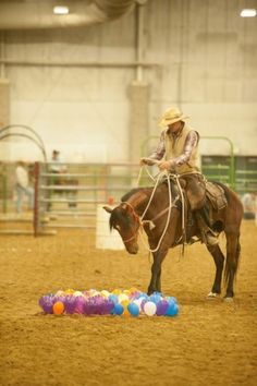 a man riding on the back of a brown horse next to colorful balls in an arena