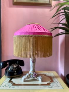 a pink lamp sitting on top of a table next to a phone and potted plant