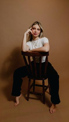 a woman sitting in a wooden chair with her hand on her head and looking at the camera