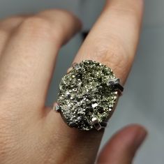 "Make a statement and give the gift of strength with our Raw Pyrite Ring. This exquisite piece showcases the bold beauty of pyrite, known for its metallic luster and protective energy. It's more than a statement piece; it's a meaningful gift that captures the essence of confidence and resilience. 🔸 Adjustable band ring 🔸25mm stone size 🔸Color may vary according to lighting 🔸Silver filled We offer  🔸Fast shipping ( under normal conditions) 🔸Free shipping  🔸Polishing cloth ( to keep your piece shiny) 🔸Jewelry case on orders of 100€ 🔸Gift box 🎁 🔸Great customer service                                 Pyrite, often called \"Fool's Gold,\" is cherished for its reflective qualities and is believed to shield against negative energy and draw money closer to you. Its captivating shine mak Silver Crystal Ring For Healing, Gold Jewelry With Raw Stone For Promise Ring, Spiritual Gold Crystal Ring In Sterling Silver, Large Stone Crystal Promise Ring, Spiritual Large Stone Crystal Promise Ring, Unique Raw Jewelry For Gifts, Gold Crystal Ring With Large Stone For Promise, Gold Sterling Silver Rings With Large Stone, Raw Stone Crystal Promise Ring In Sterling Silver