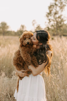 a woman in a white dress is holding a brown teddy bear and kissing her face