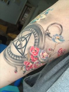 a person with a tattoo on their arm has flowers and a compass in the middle