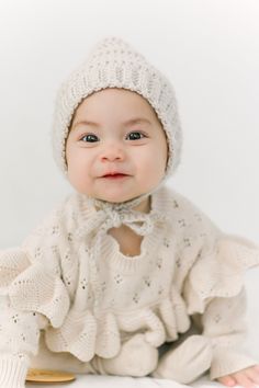 a baby wearing a knitted hat and sweater sitting on the floor in front of a white background