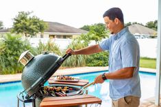 a man grilling food on top of a bbq next to a swimming pool