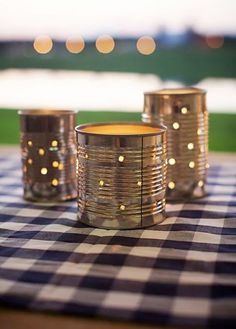 three tin can candle holders sitting on top of a blue and white checkered table cloth