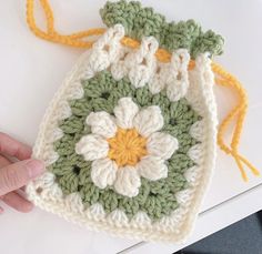 a crocheted bag with a flower on the front is being held up by a person's hand