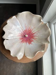 a large white flower shaped bowl sitting on top of a wooden table next to a window