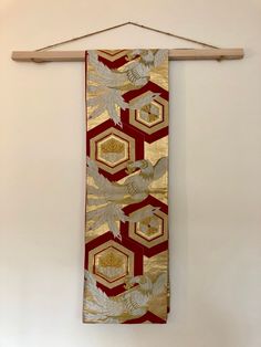 a gold and red scarf hanging on a wooden hanger next to a white wall