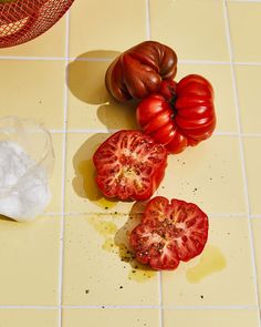 three tomatoes are on the counter and one is cut in half