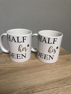 two white coffee mugs with the words half her and his open on them sitting on a wooden table