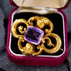 This fabulous brooch features a light purple cushion cut amethyst set into a flourished setting with engraved floral details. The purple color and the unpolished yellow gold complement each other beautifully. The pin is crafted in 10k yellow gold and is complete with a 14k gold C-clasp closure. Victorian Yellow Gold Brooches With Gemstone, Elegant Purple Gemstone Brooches, Luxury Purple Brooches For Formal Occasion, Antique Yellow Gold Brooches With Gemstone, Heirloom Yellow Gold Gemstone Brooches, Purple Gemstone Brooches For Weddings, Purple Gemstone Wedding Brooches, Elegant Amethyst Brooches For Wedding, Art Nouveau Formal Jewelry Brooch