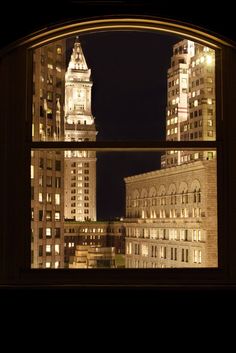 the view from an open window at night with lights on and buildings in the background