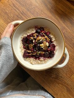 a person holding a bowl of oatmeal with fruit and nuts in it