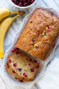 a loaf of fruit bread sitting on top of a table next to some bananas and cranberries