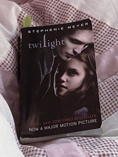 the twilight saga book is laying on top of a bed with pink sheets and checkered comforter