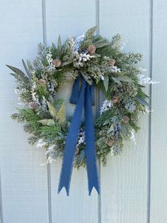 a wreath hanging on the side of a white wall with blue ribbon and pine cones