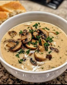 a bowl of soup with mushrooms and parsley in it next to a piece of bread