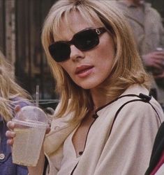 a woman wearing sunglasses and holding a drink