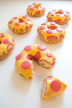 several donuts with yellow icing and pink polka dots are arranged on a white surface