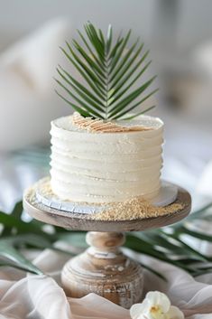 a white cake sitting on top of a wooden stand next to a flower and palm leaf