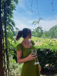 a woman in a green dress holding a wine glass and looking up at the sky