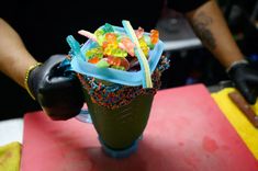 a cup filled with lots of gummy bears on top of a red table next to a pair of gloves