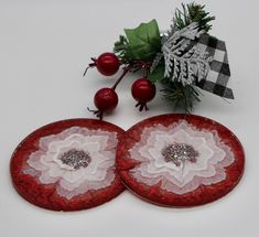 two red plates with white flowers on them next to holly branches and berries in the background