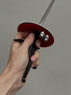 a hand holding a pair of scissors in front of a red umbrella with black handles