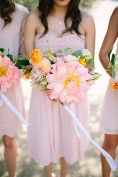 three bridesmaids in pink dresses hold bouquets of flowers and ribbons as they walk down the aisle