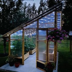 a small greenhouse with plants growing in it and lights on the side of the building