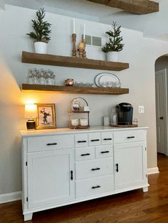 a kitchen with white cabinets and wooden shelves on the wall above them is lit by a lamp