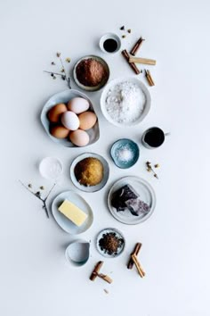 an assortment of ingredients are arranged in bowls on a white surface with cinnamons, eggs and spices