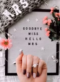 a woman holding her hand up to the camera with flowers in front of her and a sign that says goodbye, miss hello mrs