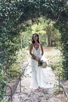 a woman in a white dress is standing under an arch with greenery on it