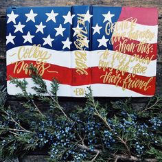 an american flag made out of wood with gold lettering on it and blue berries in the foreground