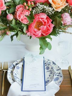 a vase filled with pink and orange flowers sitting on top of a table next to a plate