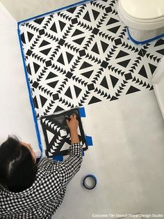 a man is painting a wall with black and white geometric designs on the floor next to a toilet