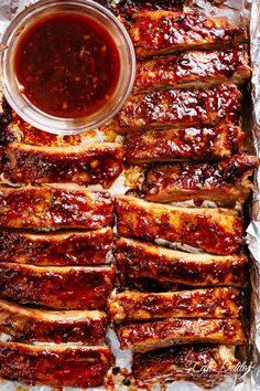 ribs covered in bbq sauce and sitting on tin foil next to a bowl of barbecue sauce