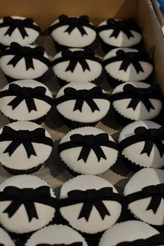 cupcakes with black bows and white frosting in a box